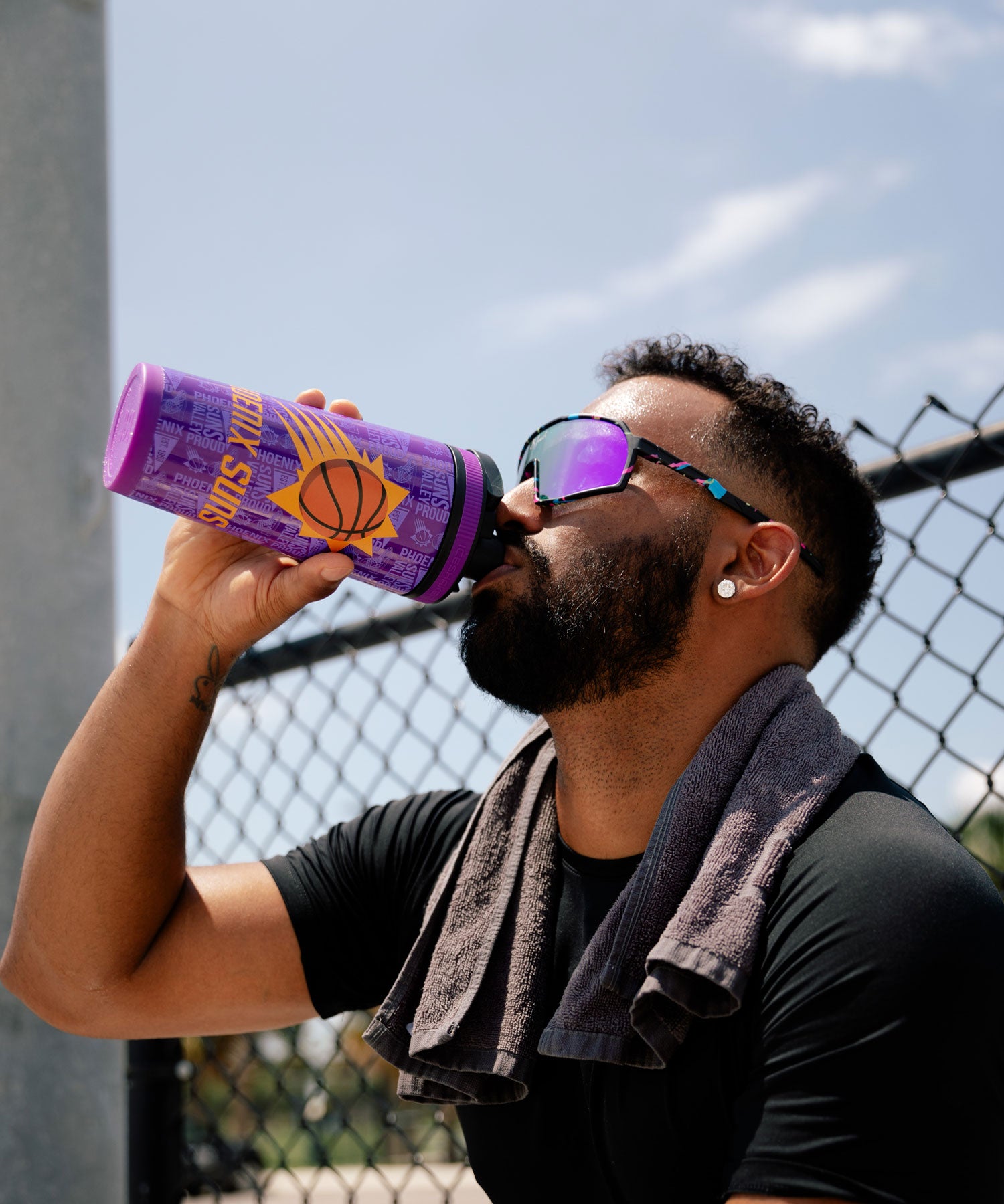 An African-American man with sunglasses on is taking is drink from a Phoenix Suns 4D Ice Shaker Protein Shaker Bottle.