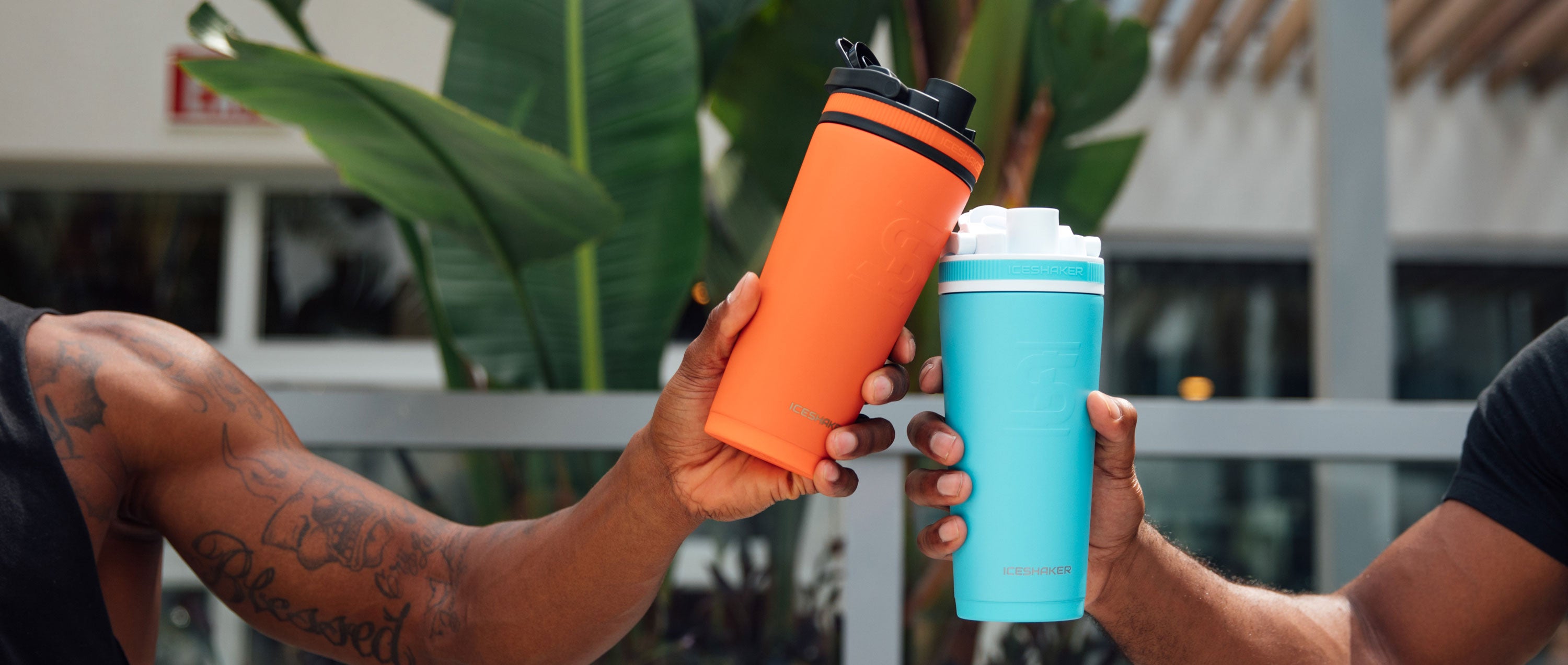 An image of the Orange 26oz Ice Shaker & Caribbean Blue 26oz Ice Shaker next to each other in an outdoor, summer setting