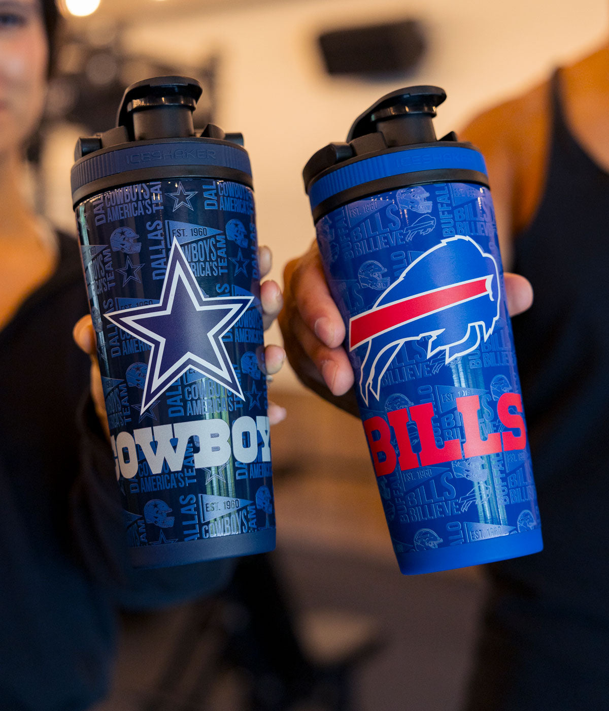 Two people standing next to each other. One is holding a Dallas Cowboys 4D Ice Shaker. The other is holding a Buffalo Bills 4D Ice Shaker.